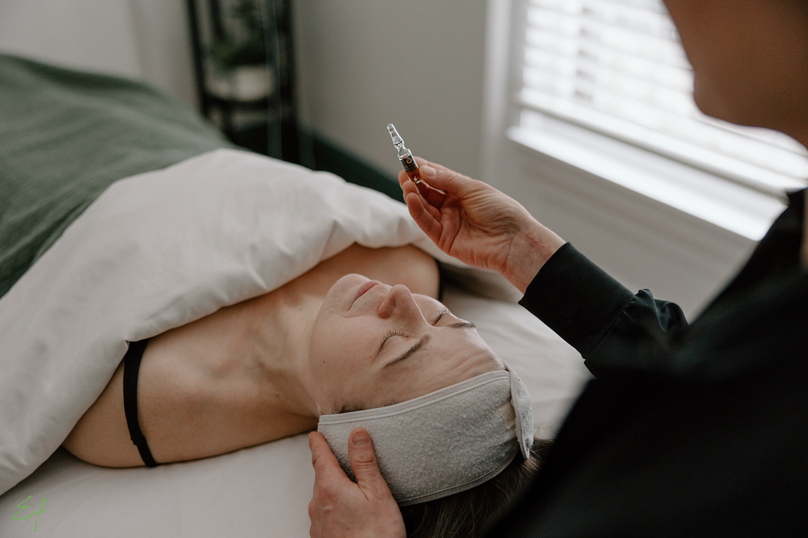 Bio-Therapeutic Facial in progress. An esthetician holds a vial of BT Cocktail as a client anticipates a facial treatment.