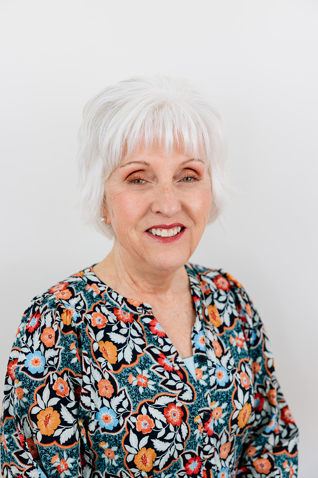 A mature smiling woman in a floral print shirt.